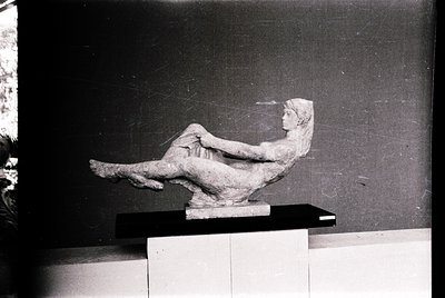 Classic black-and-white sculpture of reclining female figure in dynamic pose, seated on a low pedestal. Minimalist compositio...