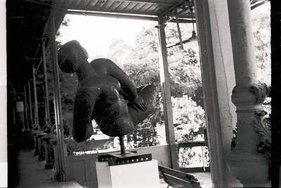 Black-and-white shot of a person mid-air performing a handstand on a wooden beam, likely in a gym or training facility. The s...