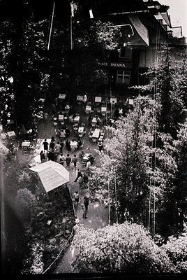 Aerial view of a bustling courtyard in a European city, likely 1950s–1960s. Crowded with tables, chairs, and people gathered ...