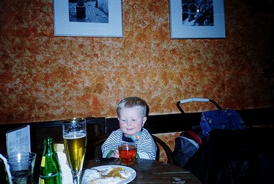 Young child seated at a rustic wooden table in a dimly lit, vintage-style café. Textured wallpaper with abstract orange patte...