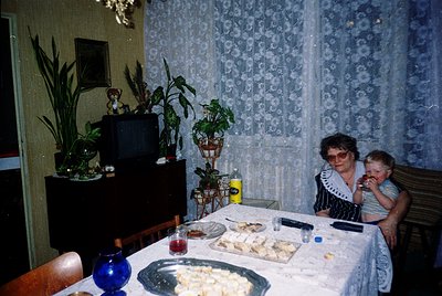 Vintage indoor scene featuring two adults seated at a table laden with food (meat pies, bread, drinks) in a mid-century home....