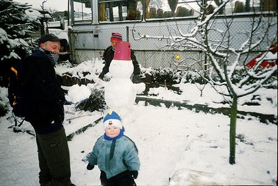 Vintage winter scene featuring a man and two children in a snowy backyard. The man wears a dark jacket and cap, while the chi...