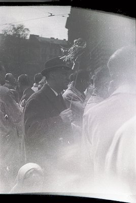 Black-and-white street scene featuring a man in a fedora playing a saxophone, surrounded by a crowd. Urban setting with visib...