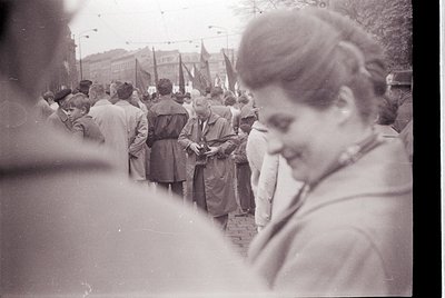Black-and-white street scene featuring a dense crowd holding flags and banners, likely a public demonstration or parade. Part...