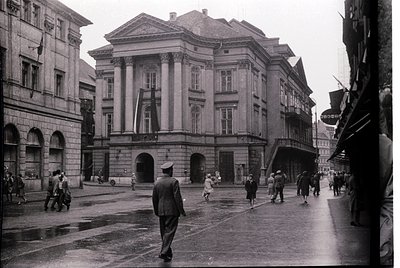 Neoclassical building with prominent columns and arched entrance in a European city square, mid-20th century. Uniformed offic...