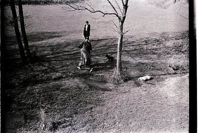 Black-and-white mid-20th century photo of three figures walking along a rural path beside a body of water. The man in the cen...