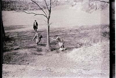 Vintage black-and-white photo capturing three children playing in a rural field, mid-20th century. One child leans into a tre...