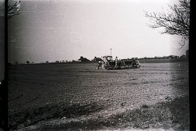 Vintage black-and-white photo of a mid-20th century tractor plowing an open field, likely post-WWII agricultural expansion. D...