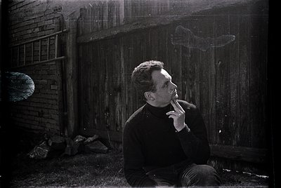 Mid-20th century man in a dark sweater sits on a brick step, brushing teeth with a manual toothbrush. Weathered brick wall an...