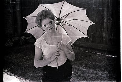 Vintage black-and-white portrait of a woman holding a large, open parasol with a sleek metal frame. She wears a sleeveless to...