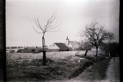 Black-and-white rural scene featuring a small church with a steep gable roof and bell tower, surrounded by leafless trees and...