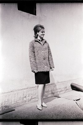 Young woman in a mid-century mod dress and cardigan poses outdoors, 1960s. Minimalist urban backdrop suggests city architectu...