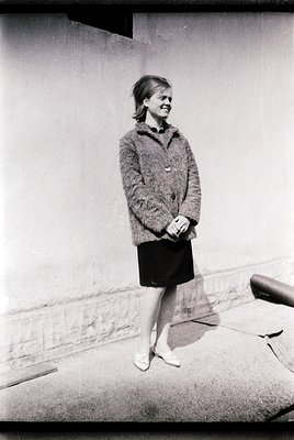 1960s fashion portrait: Woman in a cardigan and pencil skirt poses against a plain wall. Mid-century hairstyle and minimalist...