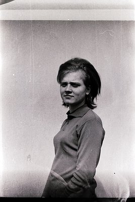 Portrait of a young woman with short, textured hair in a 1970s-style sweater, standing against a plain wall. Vintage film gra...
