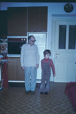 Mid-century kitchen interior featuring built-in wood cabinetry and a built-in oven. A man in a light sweater and glasses stan...