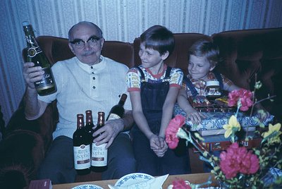 Vintage family portrait from the 1970s featuring a man in a button-down shirt holding a bottle of *Shtilna* beer, flanked by ...