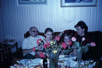 Family portrait from the 1970s–1980s featuring three generations: an elderly man in a button-down shirt, a young boy in a str...