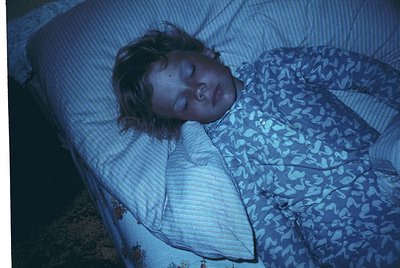 Portrait of a resting individual in a dimly lit hospital bed, draped in patterned hospital linens. The vintage blue-tinted ph...