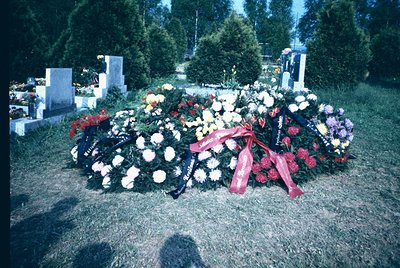 Memorial wreaths arranged on a grave in a solemn cemetery setting, featuring white roses, red carnations, and purple flowers ...