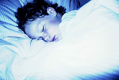 Vintage black-and-white portrait of a child peacefully sleeping under soft lighting, likely mid-20th century. The subject app...