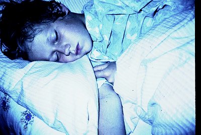 Vintage sepia-toned portrait of a child peacefully sleeping, wrapped in a patterned blanket. The soft focus and muted lightin...