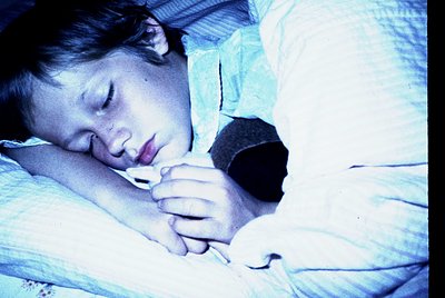Vintage sepia-toned photo of a child sleeping peacefully, clutching a dark stuffed animal. Soft bedding and dim lighting evok...