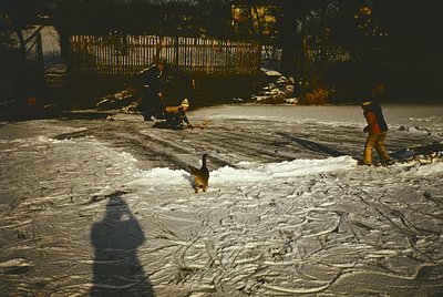 Vintage winter scene of three children playing in a snow-covered park. Snowman in progress with bundled figures in background...