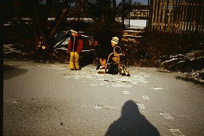 Vintage winter scene featuring two children in winter gear—one in a red jacket/yellow pants, the other in a white hat/beige c...