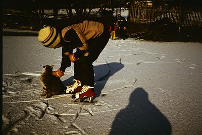 Street vendor in vintage attire (wide-brim hat, apron) tending to a small dog in a city setting, likely 1960s–1970s. Red-and-...
