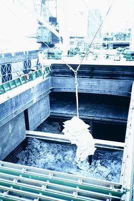 Industrial shipyard scene showing a large steel beam suspended mid-air via crane for welding or assembly. Heavy machinery and...