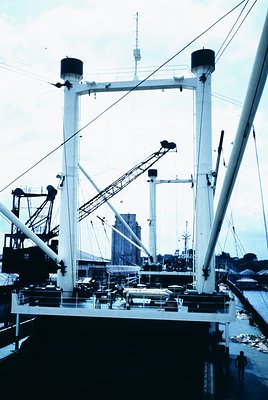 Industrial port crane vessel with two towering white A-frames and extended booms, docked at a mid-20th century port. Backgrou...