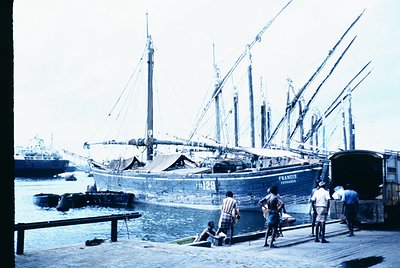 Vintage maritime scene featuring a wooden sailing ship named *Francisco* with multiple masts and rigging, docked at a port. W...