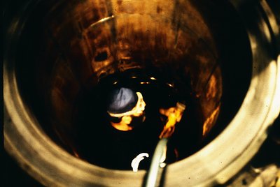 Close-up of molten glass in a furnace, captured through a viewing port. The orange-hued glass reflects light, revealing a par...