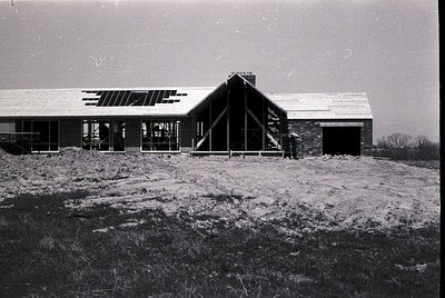Mid-century modern home under construction, featuring clean lines, large glass windows, and a flat roof with overhangs. Stone...
