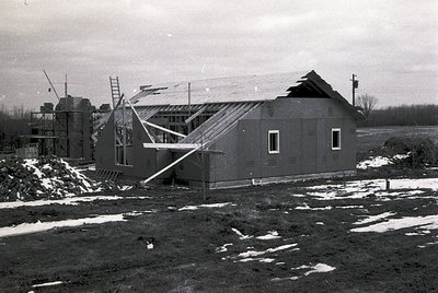 Mid-century modern house under construction, featuring exposed roof trusses and unfinished concrete block walls. Snow patches...