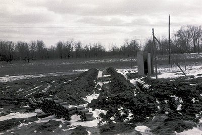 Cold winter landscape with exposed construction site. Piles of dirt and stacked concrete blocks beside a small concrete shelt...