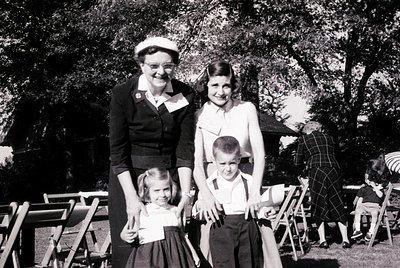 Family portrait from the 1950s–1960s, featuring a woman in a sailor-style blouse and hat holding a young girl, with a boy sta...