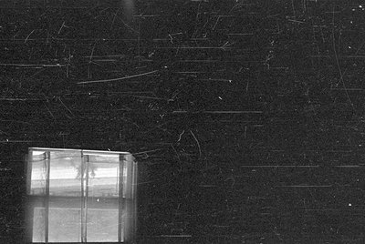 A black and white photograph showing a multi-pane window in the lower left corner. The rest of the frame is filled with a dar...
