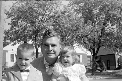A black and white photograph of a man and two children. The man wears a suit and bowtie, the young boy wears a suit and bowti...