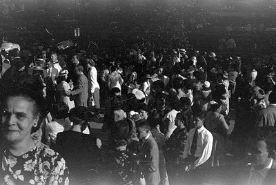 A large crowd of people gathered in a dimly lit indoor space. Many individuals are wearing formal attire, including suits, ti...