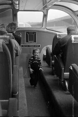 Interior of a passenger vehicle with a sign reading 'WATCH YOUR STEP'. A young boy in overalls stands in the aisle, while two...