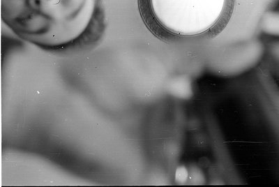 Blurred black-and-white photo showing a partial, indistinct human face and upper torso, with a circular light source (e.g., w...