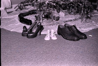 Three pairs of shoes—black high heels, white sneakers, and black dress shoes—placed on a carpeted floor in front of a decorat...