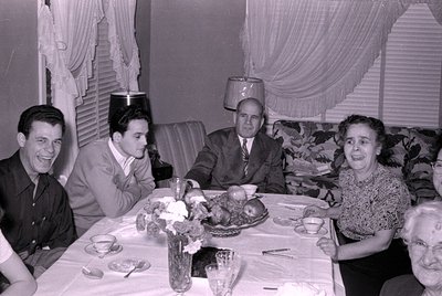 Six people seated around a table set with floral centerpieces, wine glasses, and plates in an indoor dining setting, likely m...