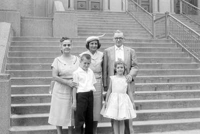 A black and white photograph of a man, two women, and two children posing on a wide set of stone stairs. The man wears glasse...