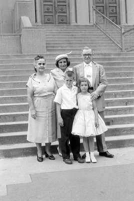 A black and white group portrait of five people standing on wide stone steps in front of a building with large double doors. ...