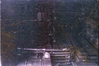 A heavily degraded photograph showing a dark, indistinct scene. The top portion contains light-colored horizontal lines and s...