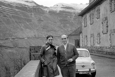 A man and a woman stand beside a white Fiat 500 with license plate S-59538. They are positioned in front of a stone building ...