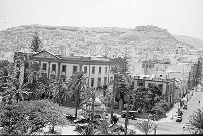 A wide shot of a city with a large neoclassical building in the foreground and a densely packed hillside of white houses in t...