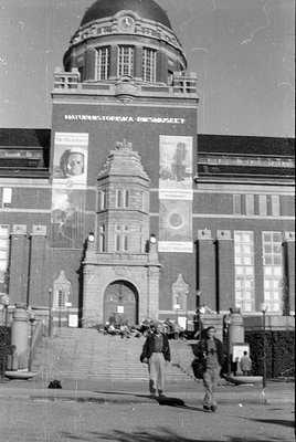 The facade of the Naturhistoriska Riksmuseet building, featuring a large dome and banners. Three people are visible in the fo...
